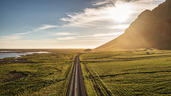 Country Road into the Sun Iceland Panorama. Empty Route 1 Country National Road, famous icelandic Ring Road Route 1 between the cities of Selfoss and Vik, along the north atlantic ocean and green icelandic mountains in summer. Aerial Drone Point of View Panorama in atmospheric sunset light. South Central Iceland, Selfoss - Vik, Iceland, Nordic Countries, Northern Europe.