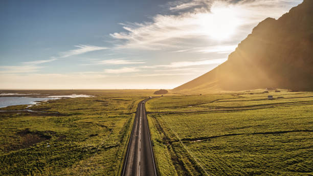 Iceland Country Road into the Sun Panorama Empty Route 1 Summer Sunset Country Road into the Sun Iceland Panorama. Empty Route 1 Country National Road, famous icelandic Ring Road Route 1 between the cities of Selfoss and Vik, along the north atlantic ocean and green icelandic mountains in summer. Aerial Drone Point of View Panorama in atmospheric sunset light. South Central Iceland, Selfoss - Vik, Iceland, Nordic Countries, Northern Europe. national road stock pictures, royalty-free photos & images