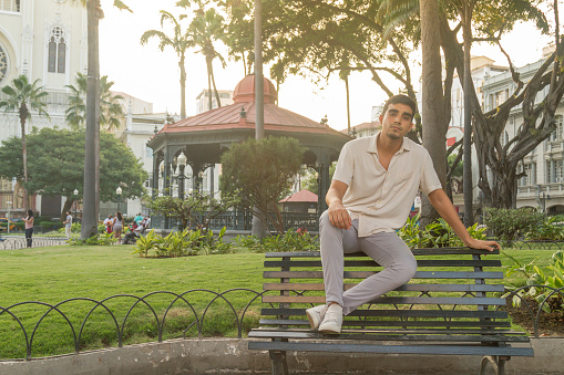 Young latin stylish ecuadorian male tourist traveling around Guayaquil, at Parque Seminario or Iguana's Park, in front of the Cathedral in Guayaquil Downtown, Guayas, Ecuador, South America. 

He's wearing a tropical white cream shirt, light grey pants and a white shoes.

Positive emotions concept.
Male Portrait concept.
Travel around Latin America.
Latin Male Portrait.