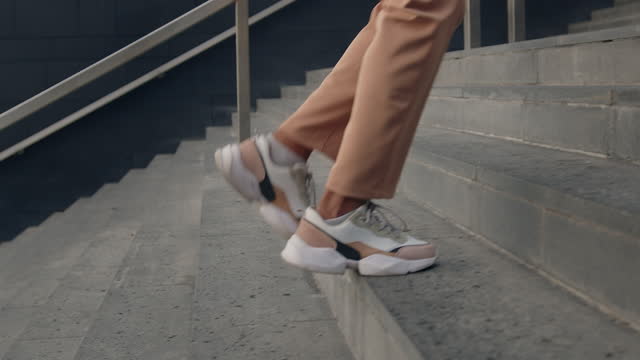 Female feet go up the stairs near business center in a modern colored sneakers