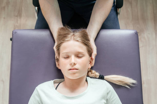 massagista realizando terapia sacral craniana em uma paciente infantil do sexo feminino e usando um toque suave para manipular as articulações no crânio ou crânio - head massage headache massaging alternative therapy - fotografias e filmes do acervo
