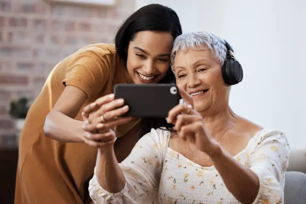 Photo of Shot of a senior woman using a smartphone to take selfies with her daughter at home