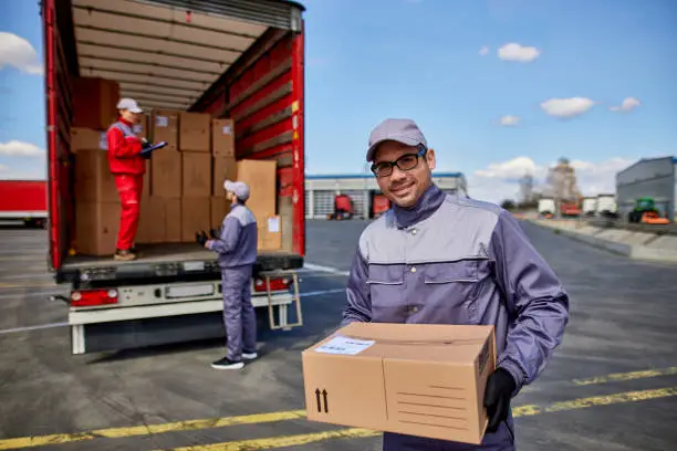 Happy delivery man with cardboard box looking at camera