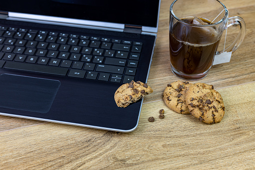 home office laptop chocolate chip cookies and tea cup on wooden table