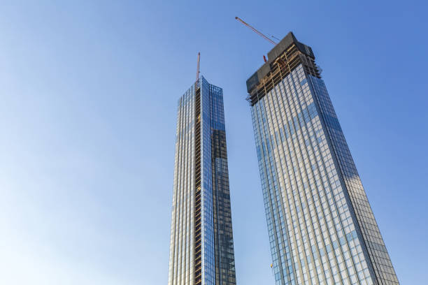 Industrial cranes and glass skyscrapers at a construction site against a bright blue sky