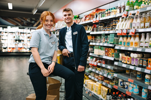 Portrait of two grocery store assistants. Male and female employees smiling at camera in supermarket.