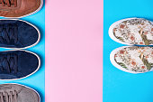 A new female's slip-ons made of floral pattern canvas and male's sneakers on a blue background with pink stripe. Flat lay. Copy space