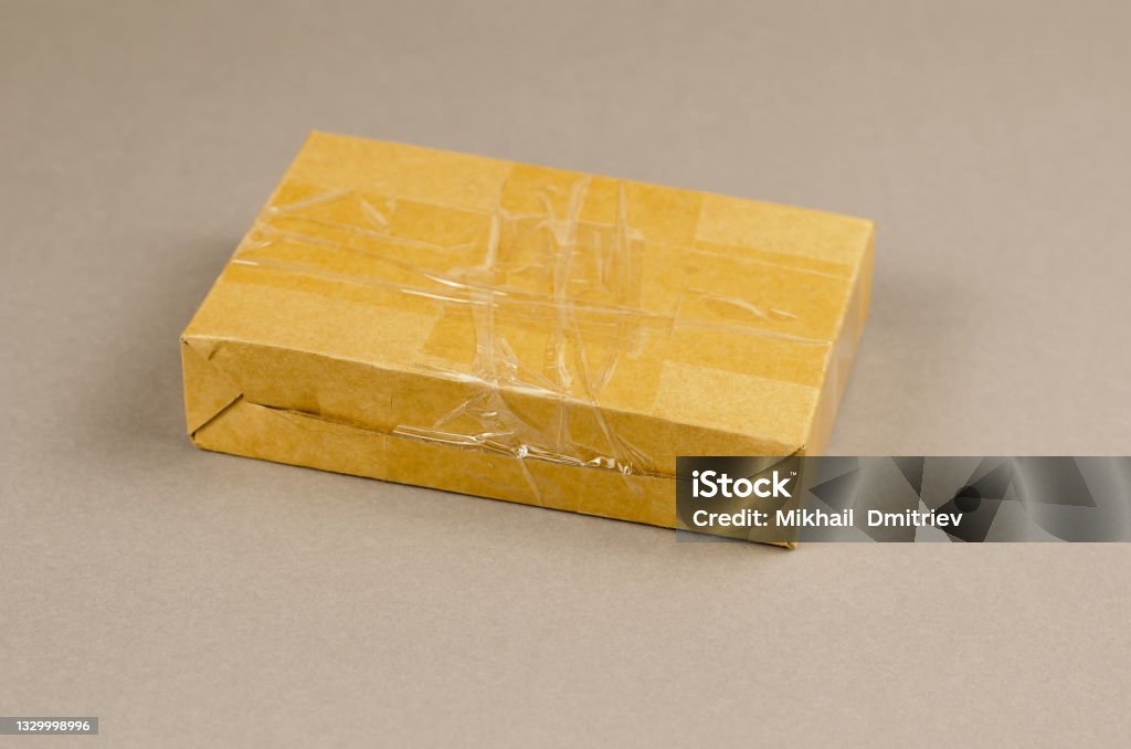 Brown cardboard box on gray background. Closed postal package wr Brown cardboard box on gray background. Closed postal package wrapped with adhesive tape. Delivery service, business. Adhesive Tape Stock Photo
