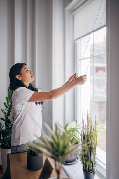 istock Woman lowering blinds on window 1329999810