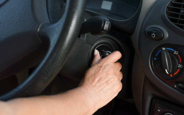 キーで車を回す成熟した女性の手のクローズアップ。高齢の女性の運転手が車の中を起動します。イグニッションキーに選択的に焦点を当てます。 - on wheels ストックフォトと画像
