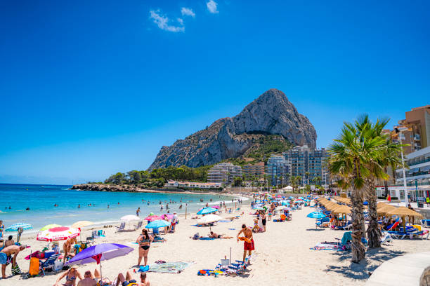 Calp, Spain. July 16, 2021. Multitude of people enjoying sun and beach with Penon de Ifach at background. Calp is a popular summer time vacation destination for tourist coming mainly from Germany and England and local retreat for Spanish.