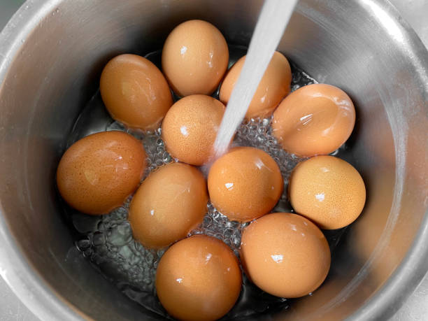 Eggs under running water Cooling freshly boiled eggs under cold running water after cooking. boiled stock pictures, royalty-free photos & images
