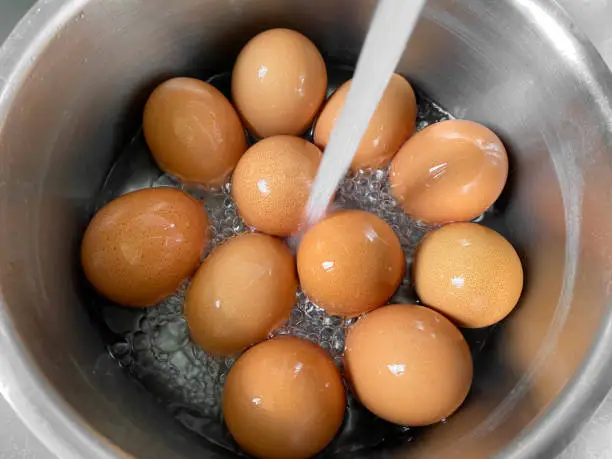 Cooling freshly boiled eggs under cold running water after cooking.