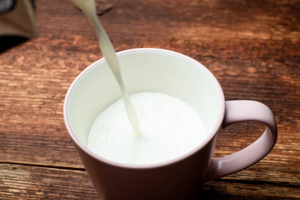 istock Milk is poured into a cup on a brown wooden background. 1330005619