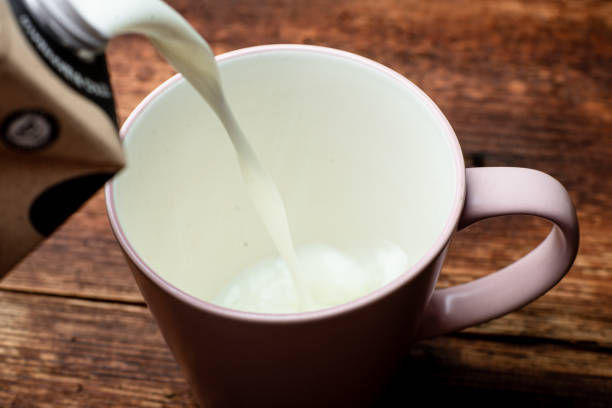 istock Milk is poured into a cup on a brown wooden background. 1330005625