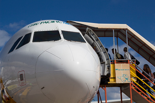 Dumaguete, the Philippines - 22 March 2018: Cebu Pacific airlines plane with passengers going in. Landed aircraft with ladder. Aircraft front view with boarding stair. Passengers onboarding by stair