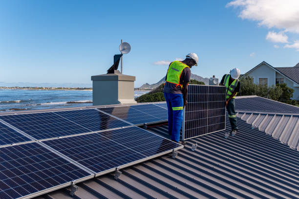 Two technicians install solar panels on a residential building Two African men install solar panels neatly on a residential roof of a house near the ocean. Sustainable living. rooftop solar stock pictures, royalty-free photos & images
