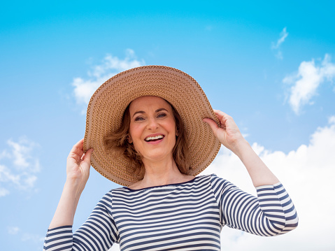 Mature woman with straw hat in the background the sea, low angle view
