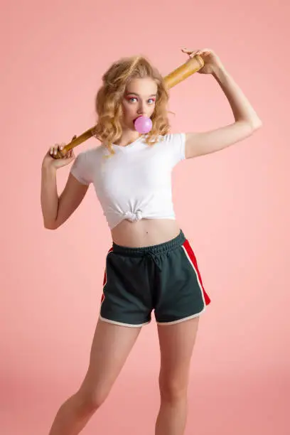 Beautiful young girl with bright makeup and hairdo in retro 90s fashion style in image of Harley Quinn isolated over pink studio background. Concept of beauty, fashion and youth, eras comparison