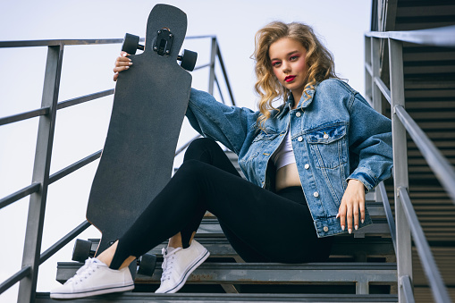 Street fashion. Beautiful adorable young girl in retro 90s fashion style, outfits posing on stairs, outdoors. Concept of eras comparison, beauty, fashion and youth. Looks excited, delighted