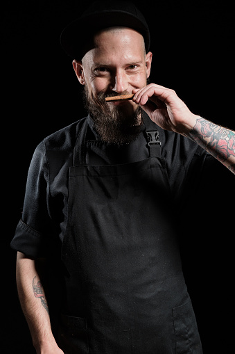 Close up portrait of chef with beard, playful smelling cinnamon stick, studio photo