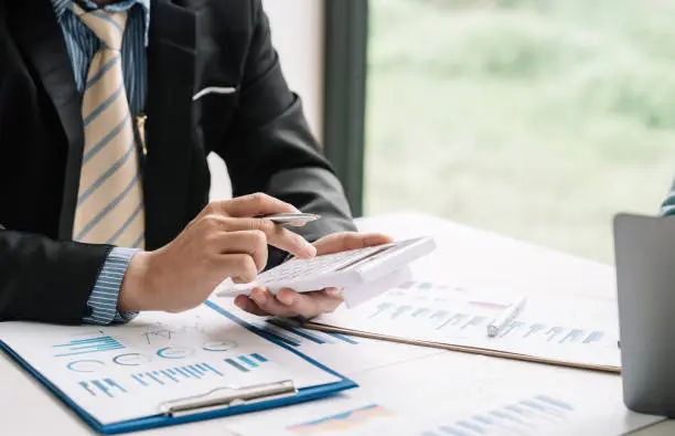 Photo of Close-up of a businessman hand holding a calculator with documents graph placed at the office desk.