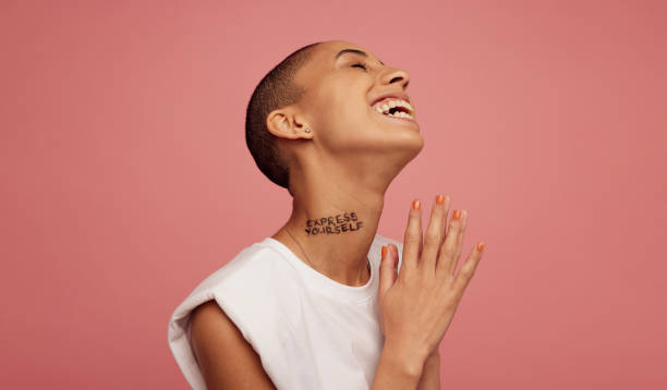 Smiling non binary female on pink background Non binary female with shaved head smiling on pink background. Androgynous woman with express yourself written on neck. completely bald stock pictures, royalty-free photos & images