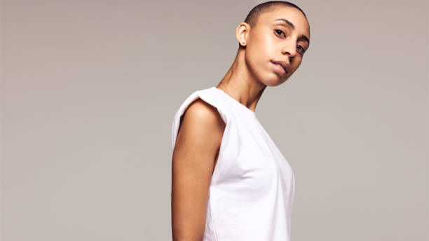 Androgynous female with shaved head Confident woman in white top staring at camera. Androgynous female with shaved head. completely bald stock pictures, royalty-free photos & images