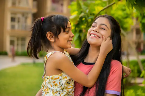 Outdoor image of happy, cheerful little girl pulling the cheeks of her aunt. They are having fun together in the fresh air.