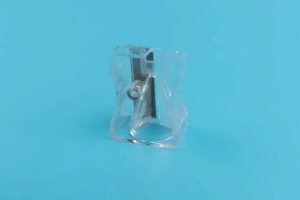Stationery, supplies for school, work in the office and creativity, transparent pencil sharpener with a metal blade, isolated on a blue background