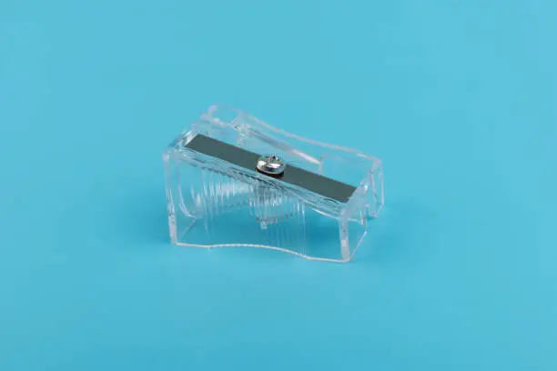 Stationery, supplies for school, work in the office and creativity, transparent pencil sharpener with a metal blade, isolated on a blue background