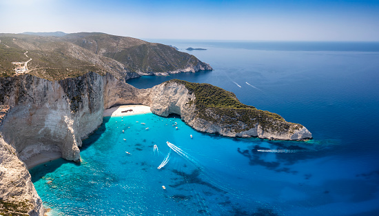 Wide aerial view to the famous Navagio shipwreck beach on the island of Zakynthos, Ionian sea, Greece, with turquoise sea and boats approaching