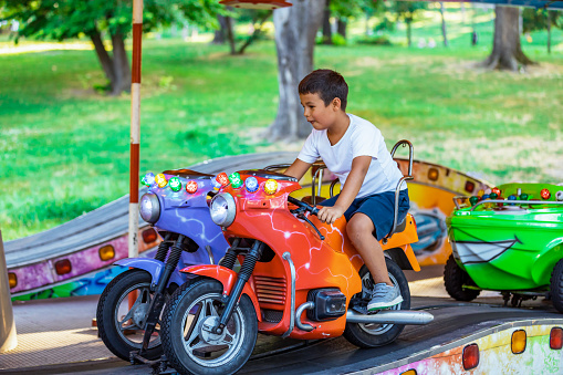 Kid playing arcade simulator machine at an amusement park. Boy enjoying motorcycle riding simulator game