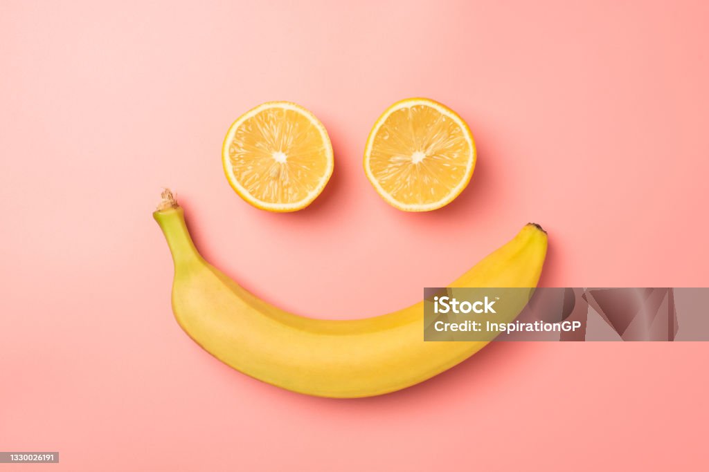 Top view photo of smiling face made from two lemon halves and banana on isolated pastel pink background Fruit Stock Photo