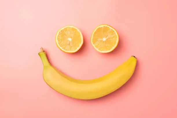 Photo of Top view photo of smiling face made from two lemon halves and banana on isolated pastel pink background