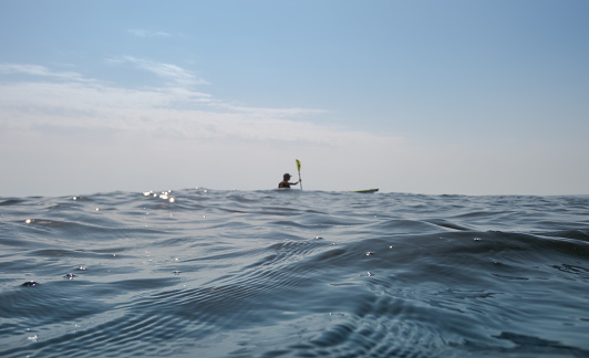 The open sea. Focus in the foreground. A man on a kayak rowing in the background