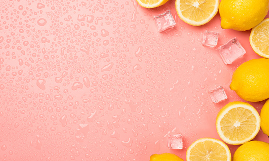 Top view photo of halves and whole yellow juicy lemons ice cubes drops on isolated pastel pink background with copyspace on the left