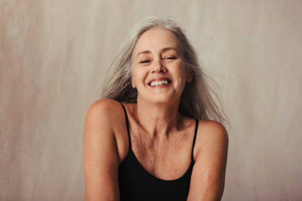 Mature woman proud of her naturally aging body Senior woman celebrating her aging body in a studio. Body positive woman wearing black underwear and smiling cheerfully. Mature woman posing against a studio background. body positive stock pictures, royalty-free photos & images