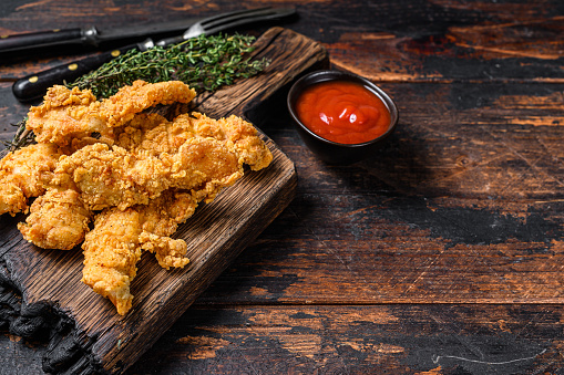 Chicken strips on a wooden cutting Board. Dark Wooden background. Top view. Copy space.
