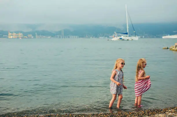 Photo of two little girls fooling around on the shore of a pebble beach near the sea