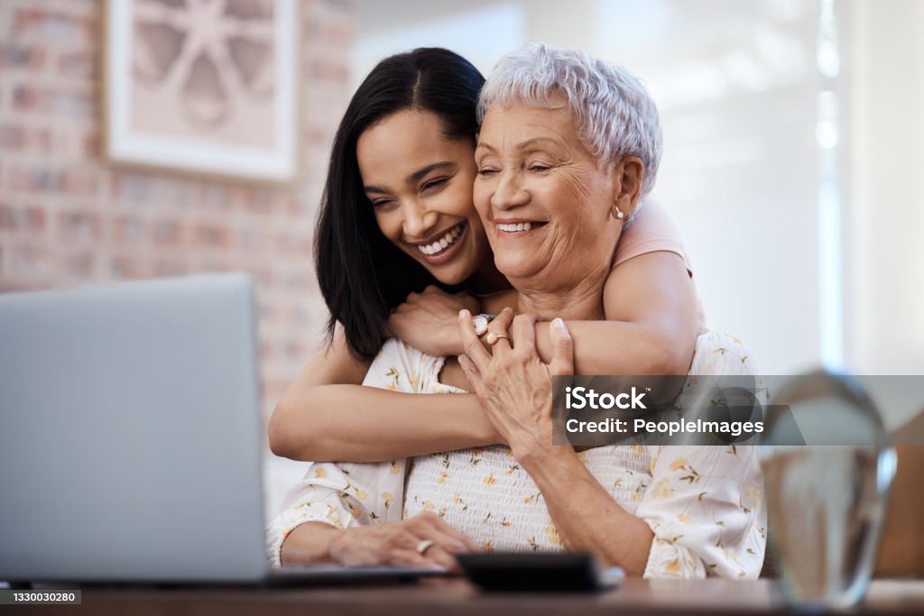 Shot of a senior woman using a laptop with her daughter at home First we save, then we have fun Senior Adult Stock Photo