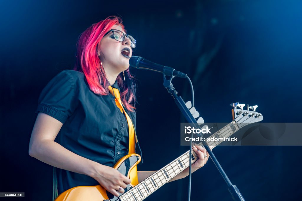 Female Bassist and Signer Performing Live A beautiful 19 year old pop punk singer and bass player performing live on stage. *inspector-headstock slightly altered in appearance* Popular Music Concert Stock Photo