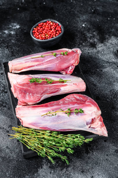 istock Raw goat shanks meat on a marble board. Black background. Top view 1330032349