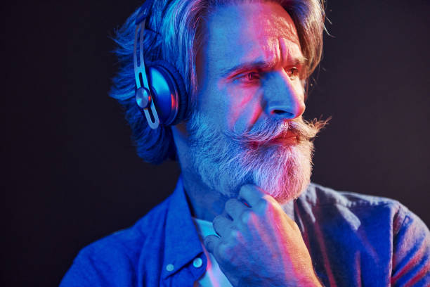 아름다운 네온 조명. 회색 머리와 수염을 가진 세련된 현대 노인은 실내에 - male beauty audio 뉴스 사진 이미지