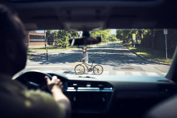 One kid crossing the road with his bike, view from inside the car