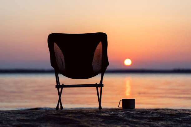 Folding camping chair with a mug of tea on the beach beautiful sunset. stock photo