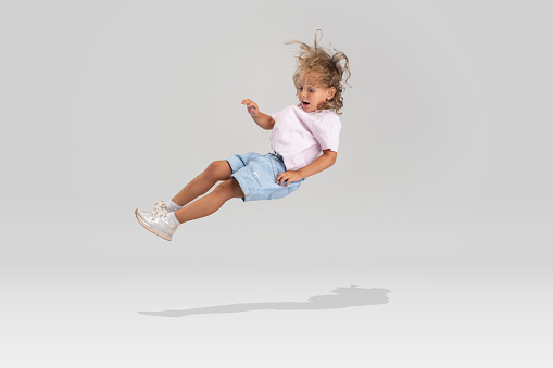 Falling to the ground. One cute little Caucasian girl in casual clothes falling down isolated over white studio background. Concept of childhood, emotions, facial expression