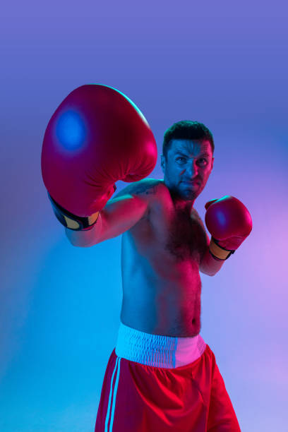 istock Close-up professional boxer in sportwear boxing on studio background in gradient neon light. Concept of sport, activity, movement, wellbeing. 1330038936