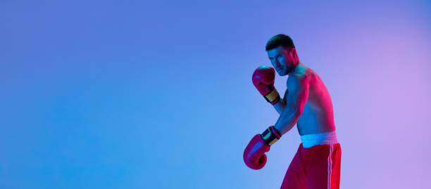 istock Flyer. One man, professional boxer in sportwear boxing on studio background in gradient neon light. Concept of sport, activity, movement, wellbeing. 1330038954