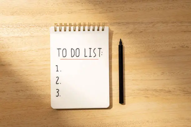 To do list in spiral notepad isolated on wooden desk. Flat lay